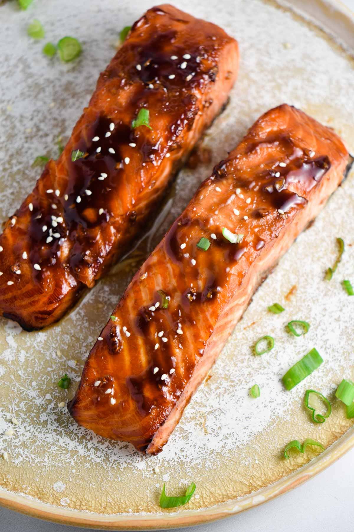Two glazed teriyaki salmon on a plate sprinkled with green onions.