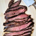 Sliced flank steak cooked medium on a cutting board.