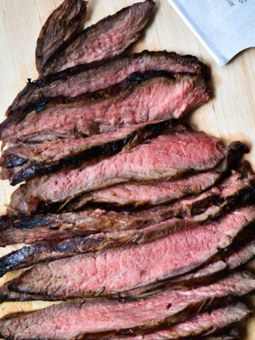 Sliced flank steak cooked medium on a cutting board.