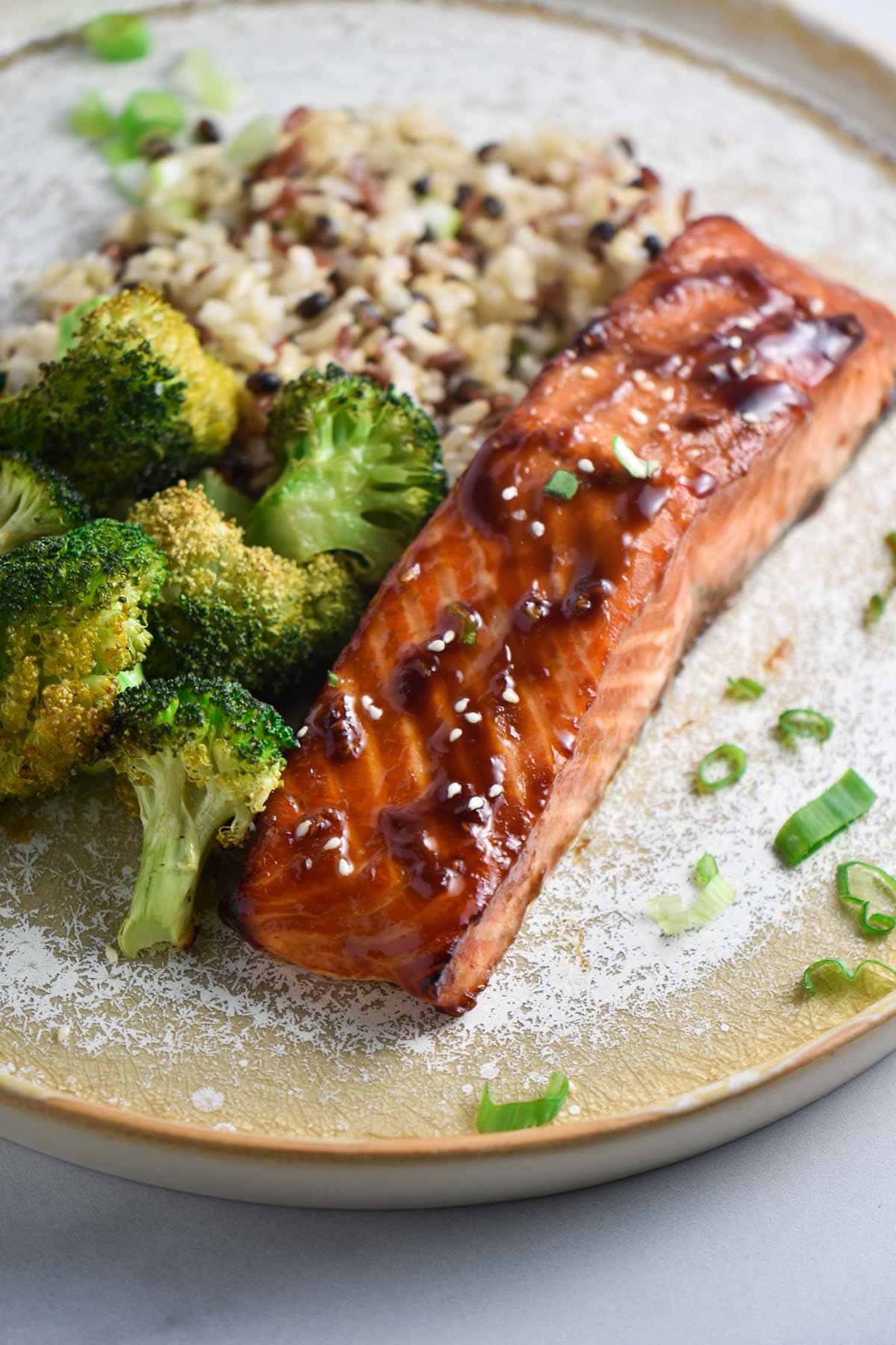 Air fried teriyaki salmon topped with a glaze and sprinkled with sesame seeds next to steamed broccoli and rice.