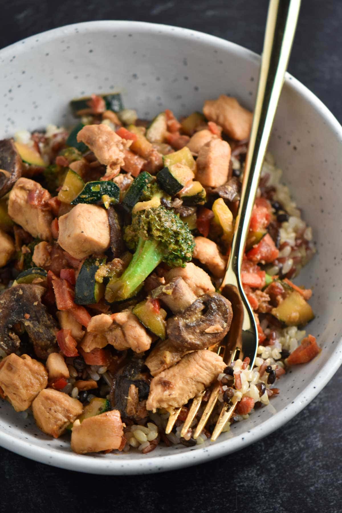 A gold fork next to a bowl of chicken stir fry without soy sauce.