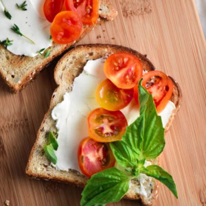 A toast smeared with cream cheese, topped with basil and tomatoes.