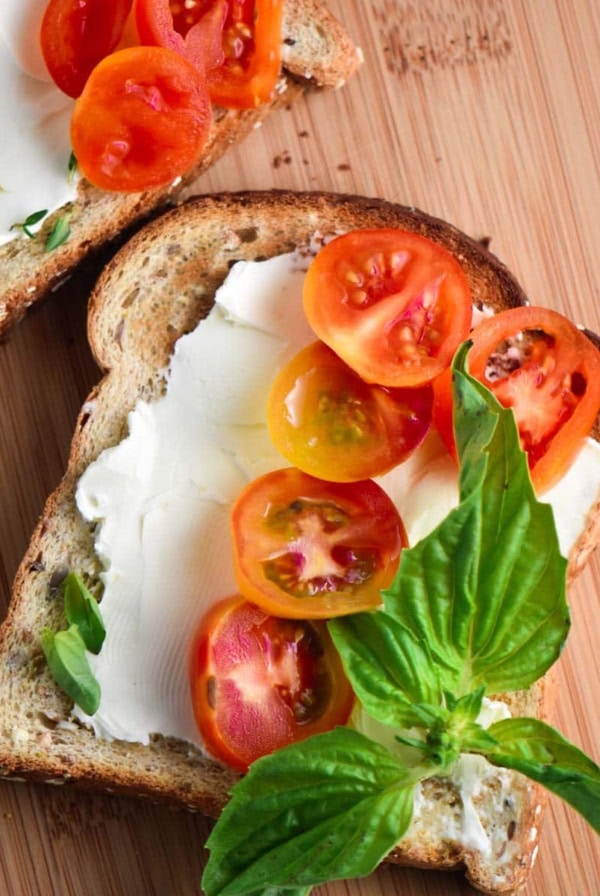 A toast smeared with cream cheese, topped with basil and tomatoes.