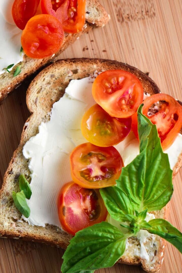 A toast smeared with cream cheese, topped with basil and tomatoes.