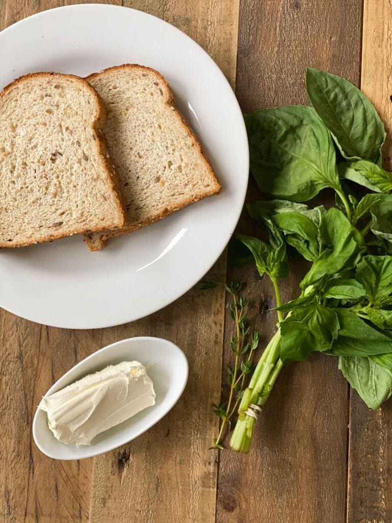 Bread, fresh herbs, and cream cheese on a wood table.