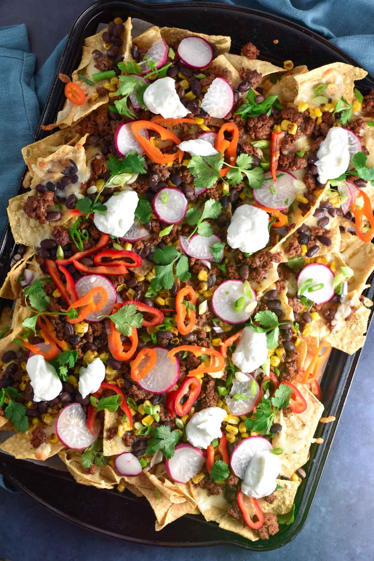 A sheet pan of nachos topped with ground beef. 