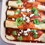 Healthy beef enchiladas in a baking dish topped with cheese and cilantro.