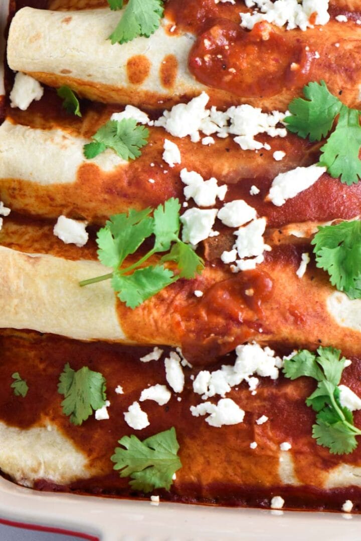 Healthy beef enchiladas in a baking dish topped with cheese and cilantro.