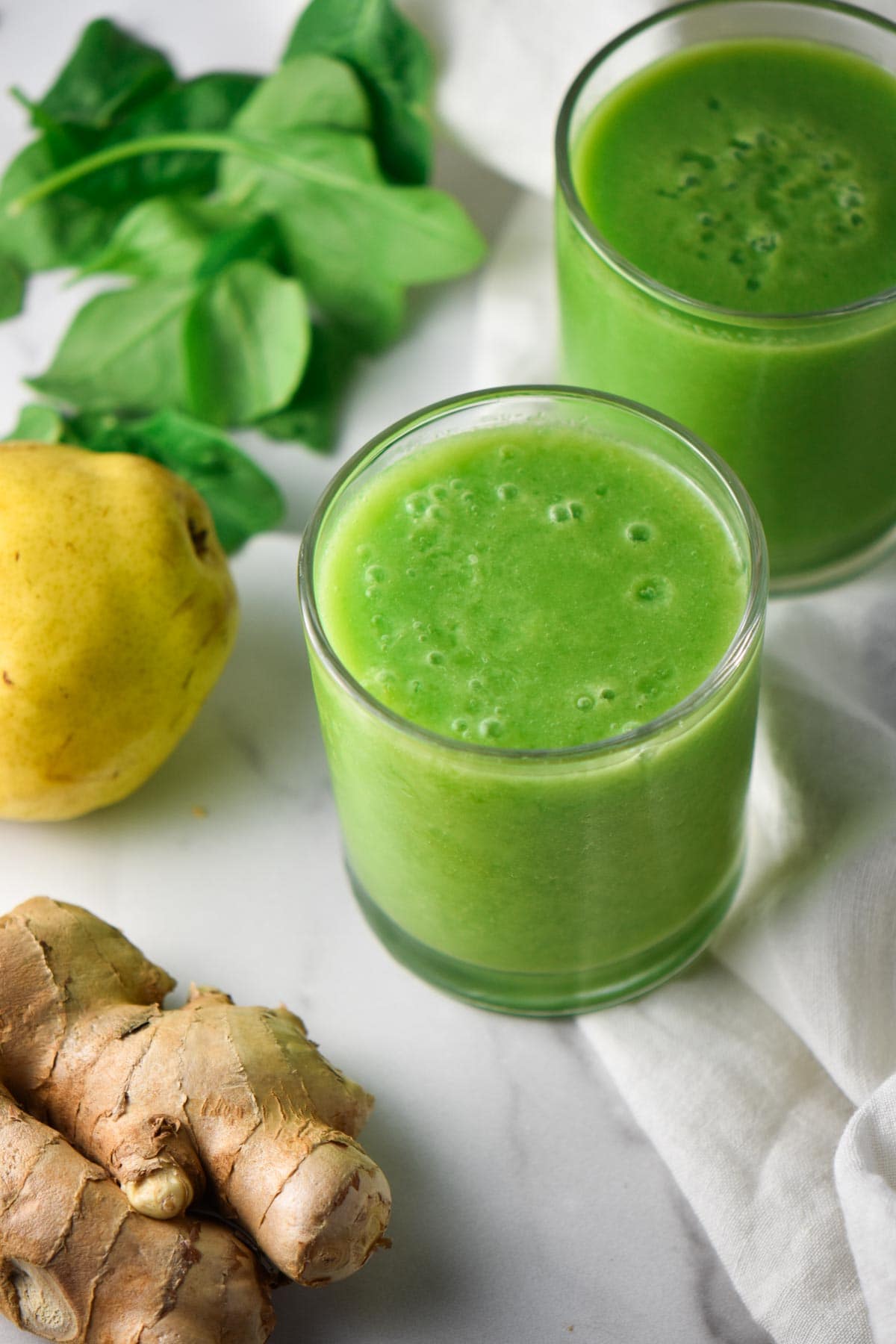 Two green anti inflammatory smoothies on a table next to spinach, ginger, and pears.