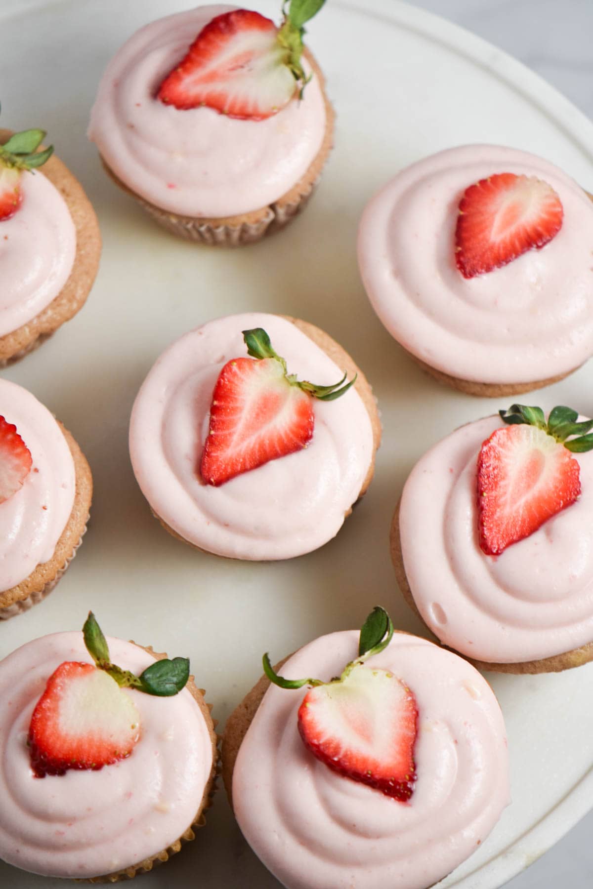 A platter with pink cupcakes topped with a strawberry.