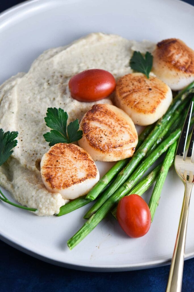 Four scallops on a plate with cauliflower and asparagus.