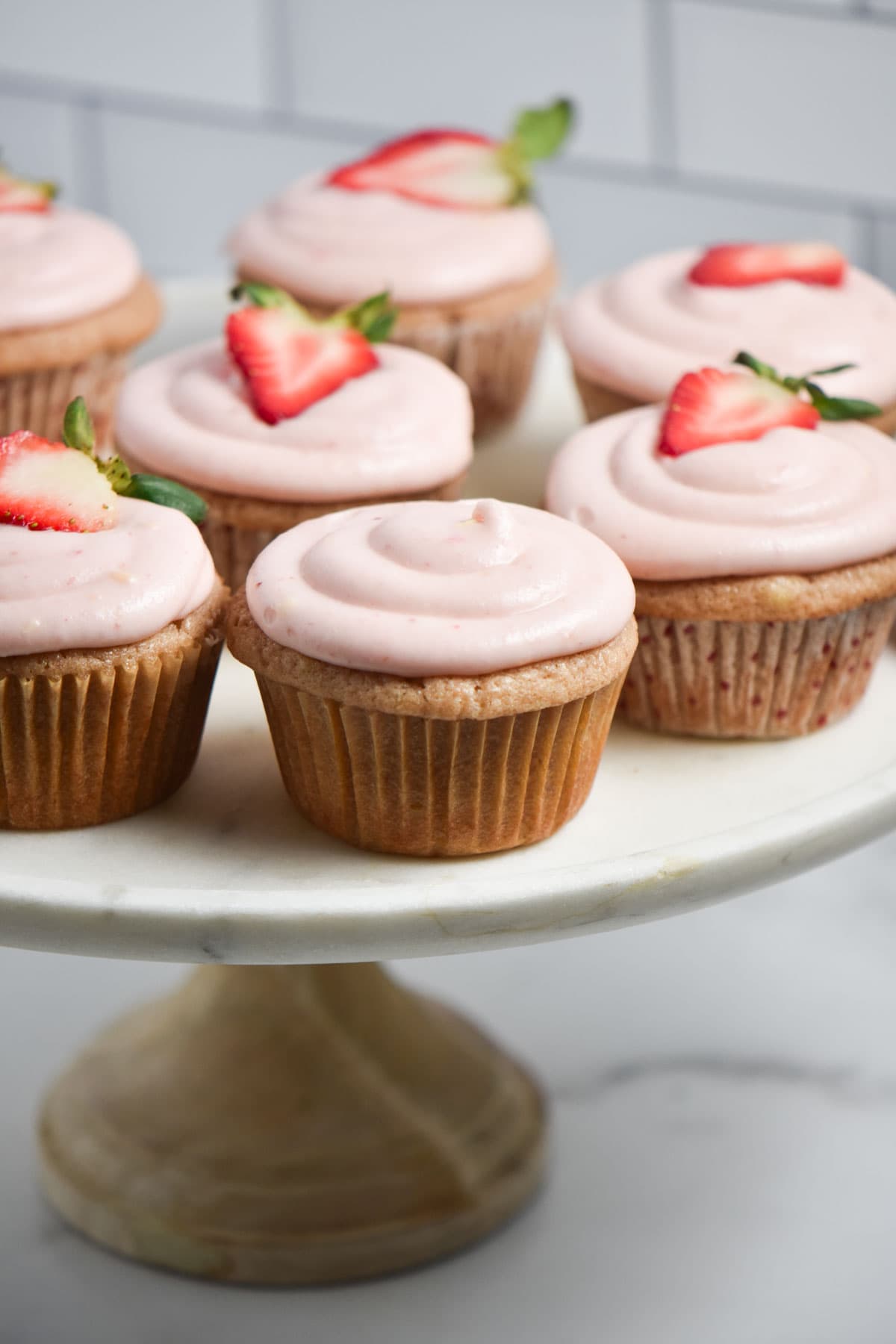 Cream cheese frosting on a cupcake, some being topped with a fresh strawberry slice.