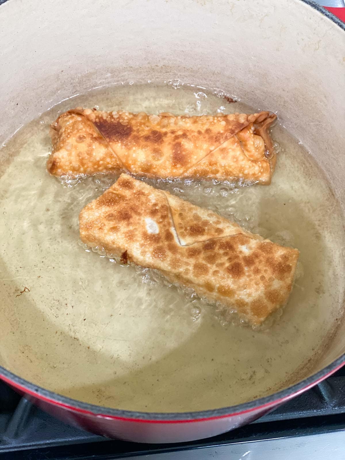Two egg rolls being fried in oil.