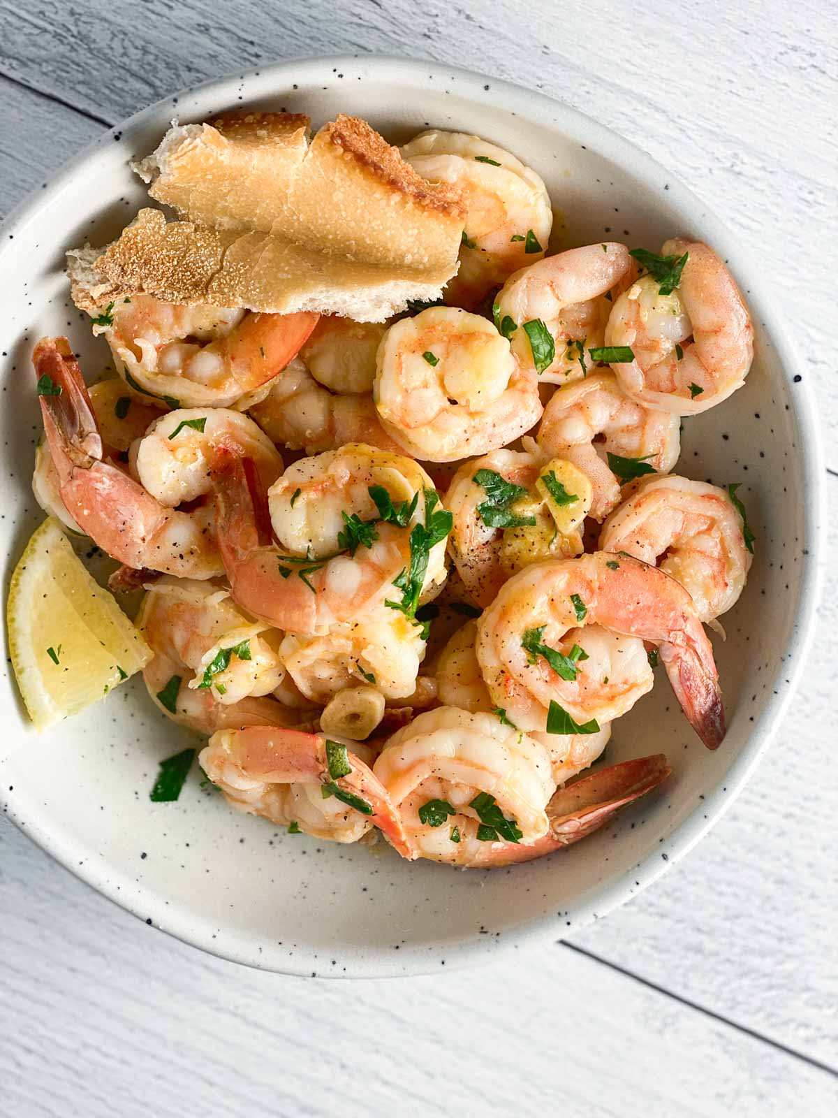 Shrimp in a white bowl with lemon, parsley, and garlic. 