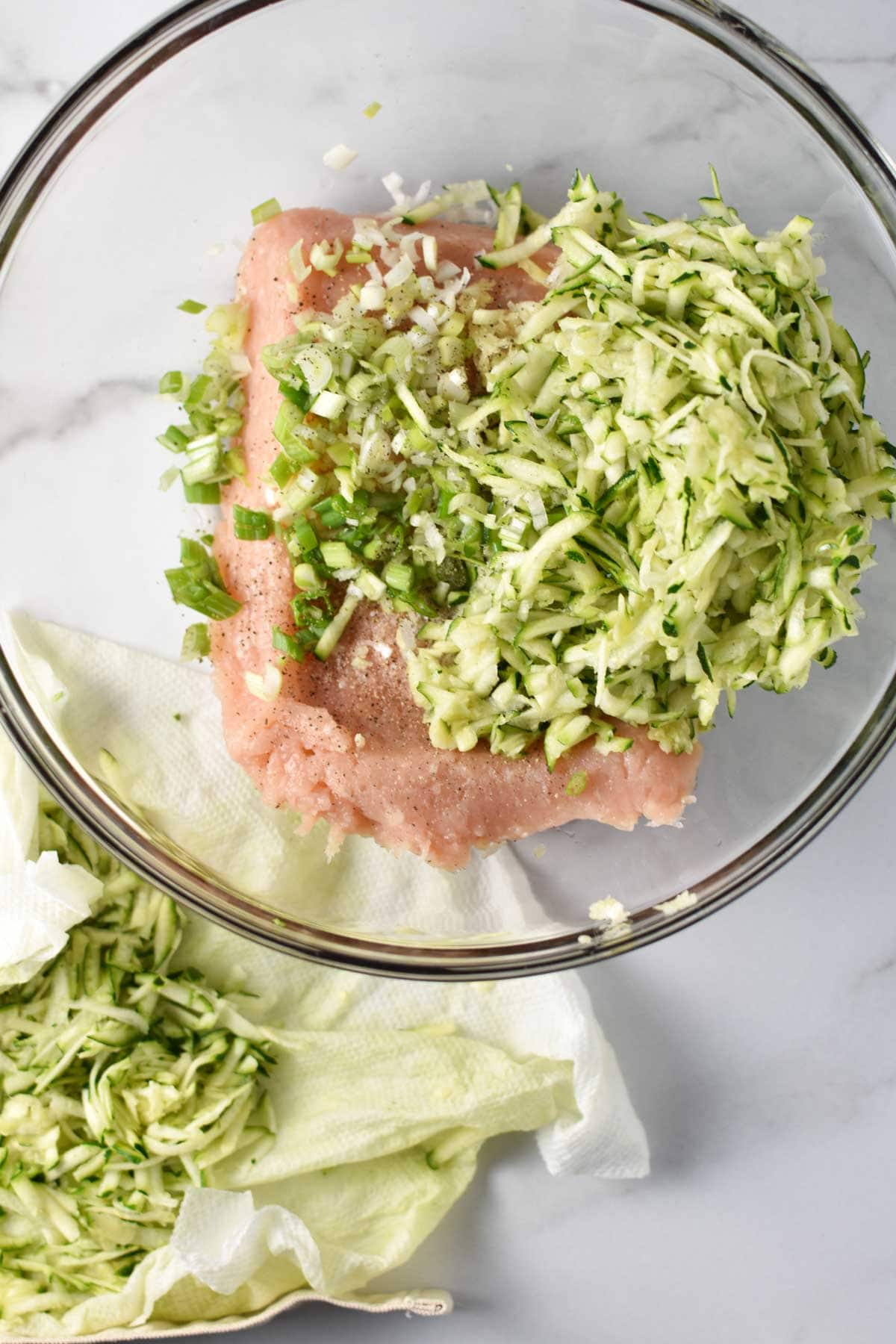 Mixing zucchini and ground chicken in a bowl.