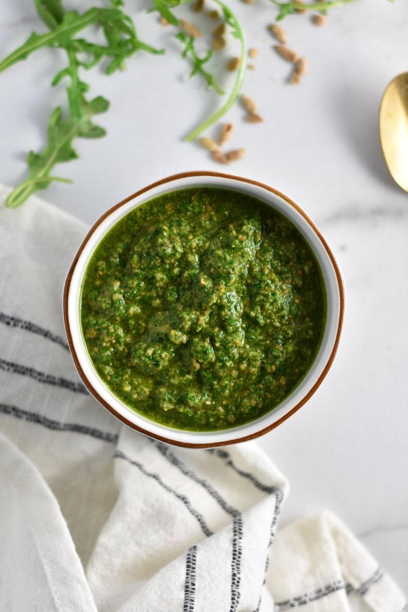 Basil pesto next to arugula and sunflower seeds.