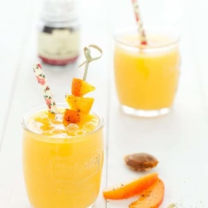Two yellow mango smoothies on a white surface.