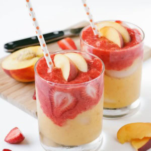 Two strawberry peach smoothies with straws.