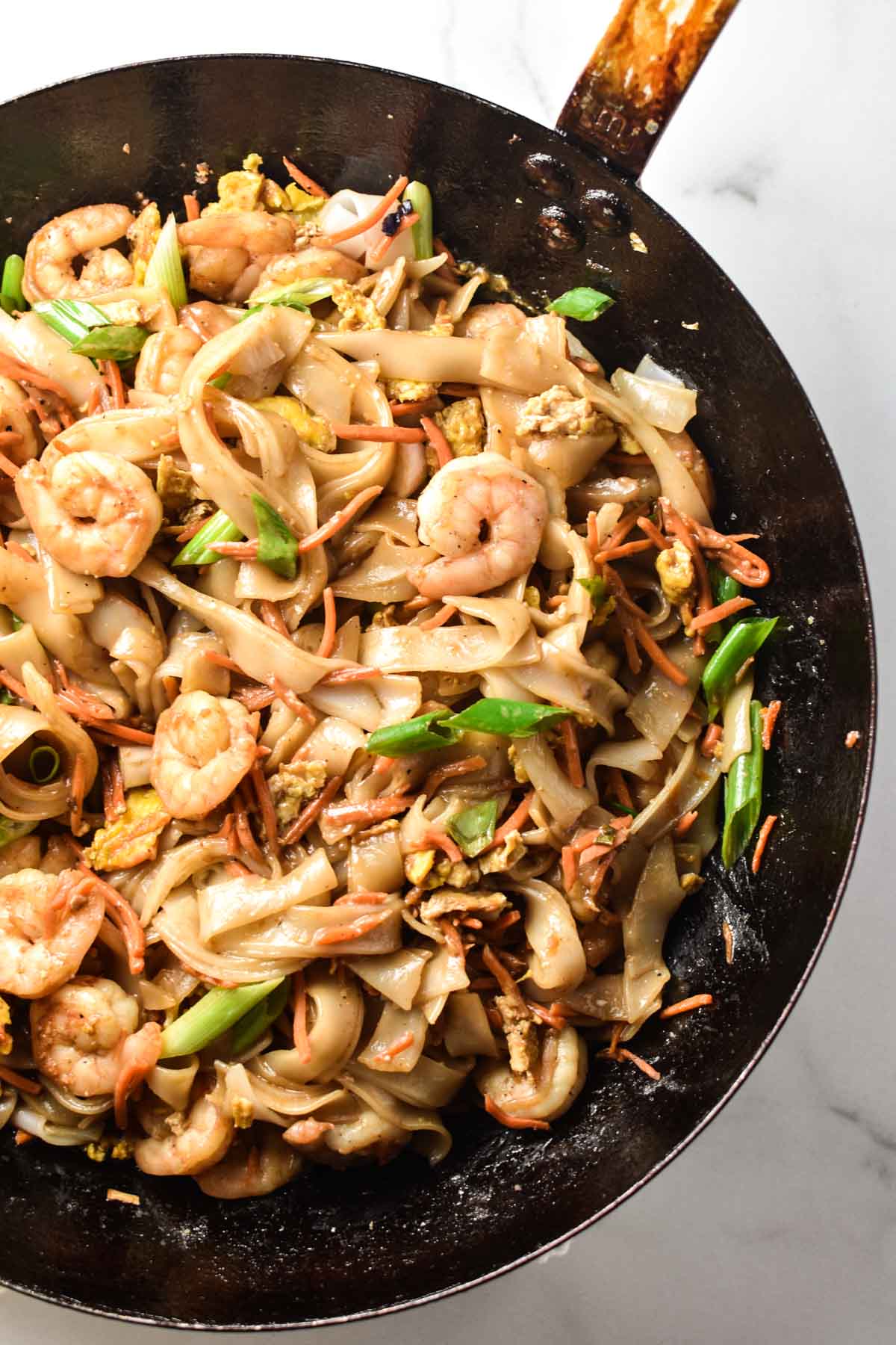 A pan with rice noodles, shrimp, and green onion.