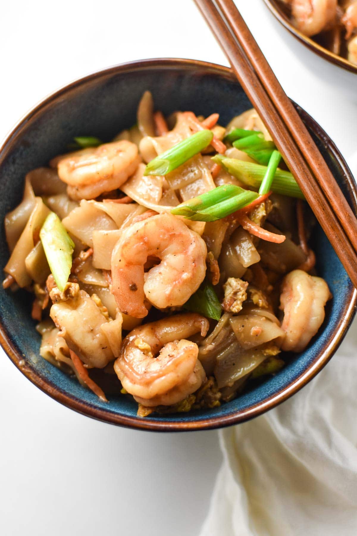 A bowl of pad Thai with green onion and shrimp.