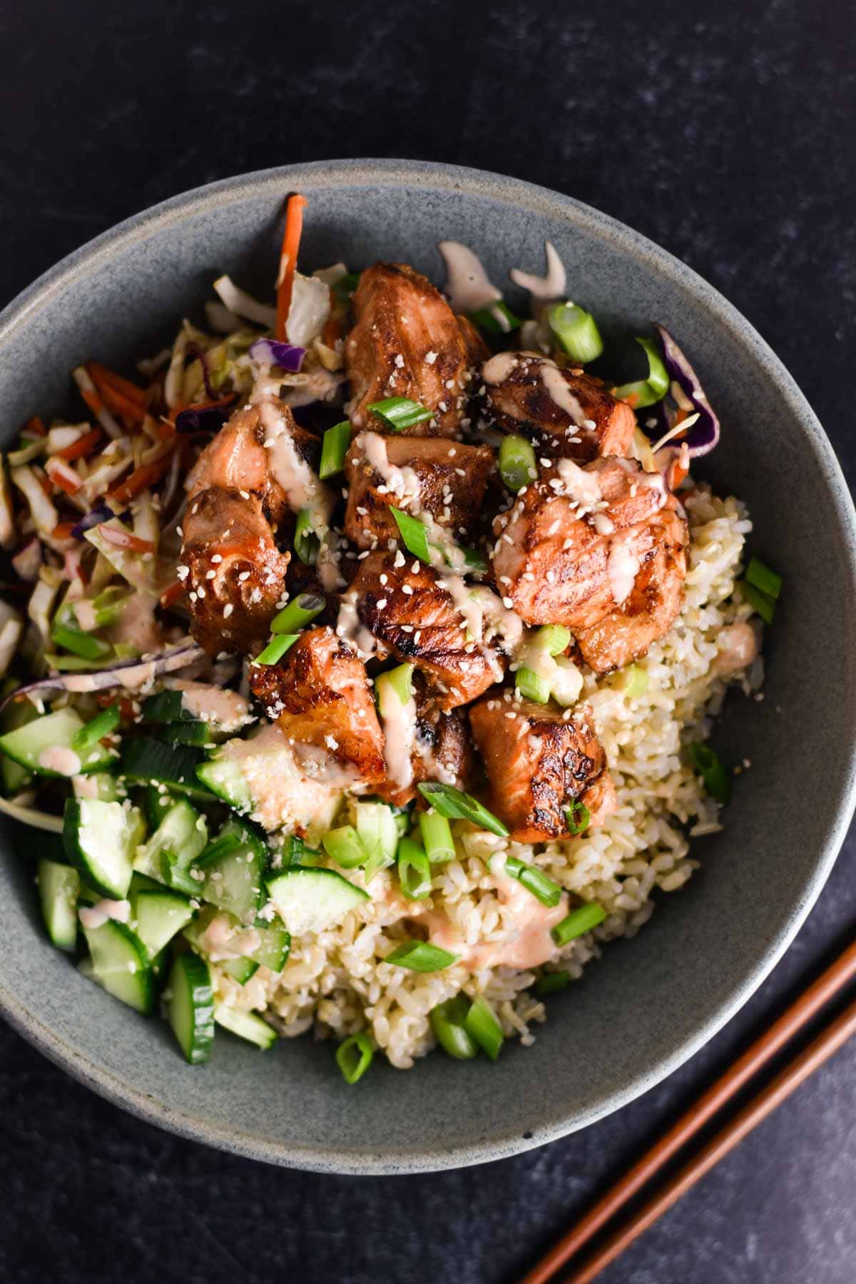 Salmon in a bowl with cucumbers and spicy mayo.