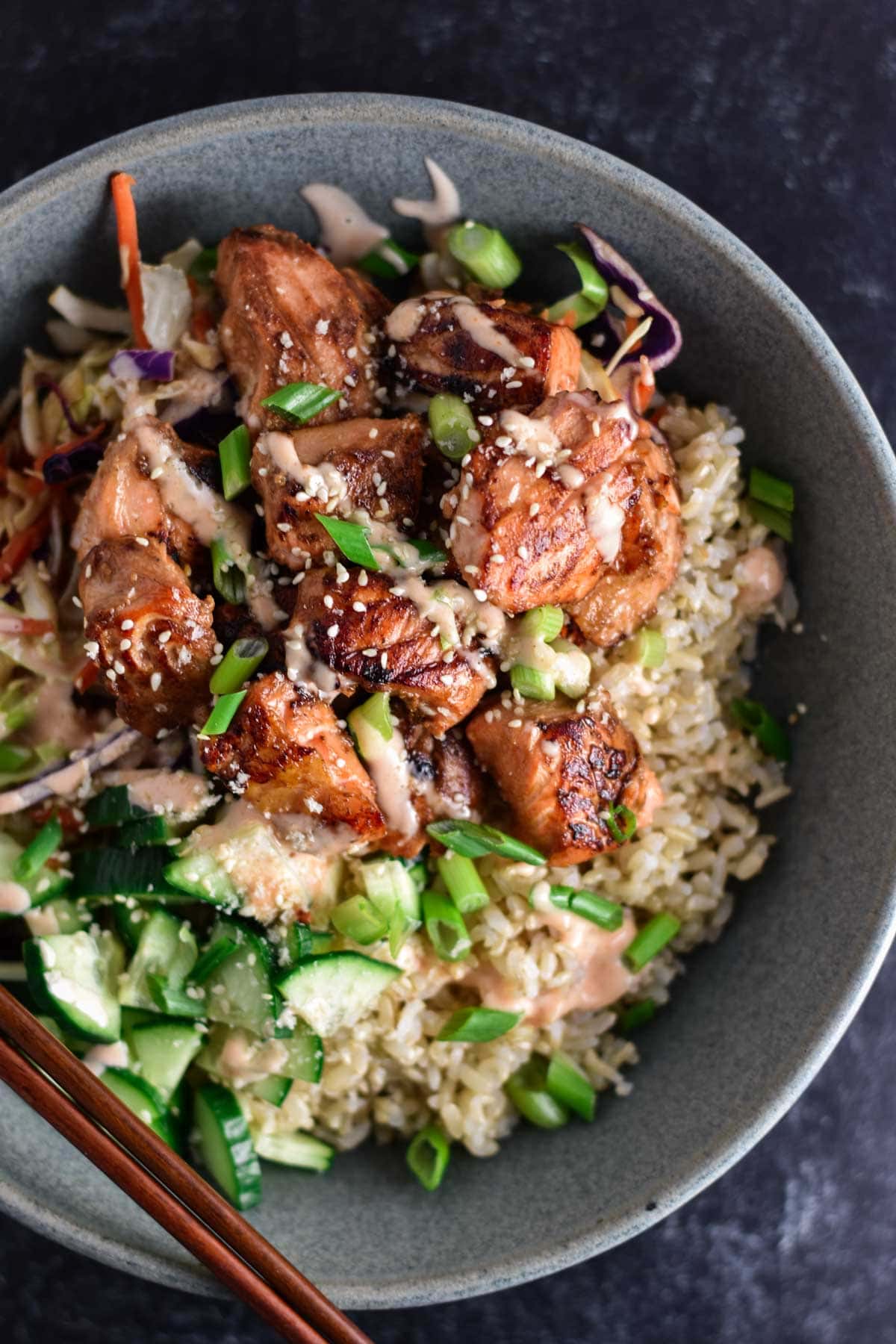 A salmon bowl with rice and chopsticks.