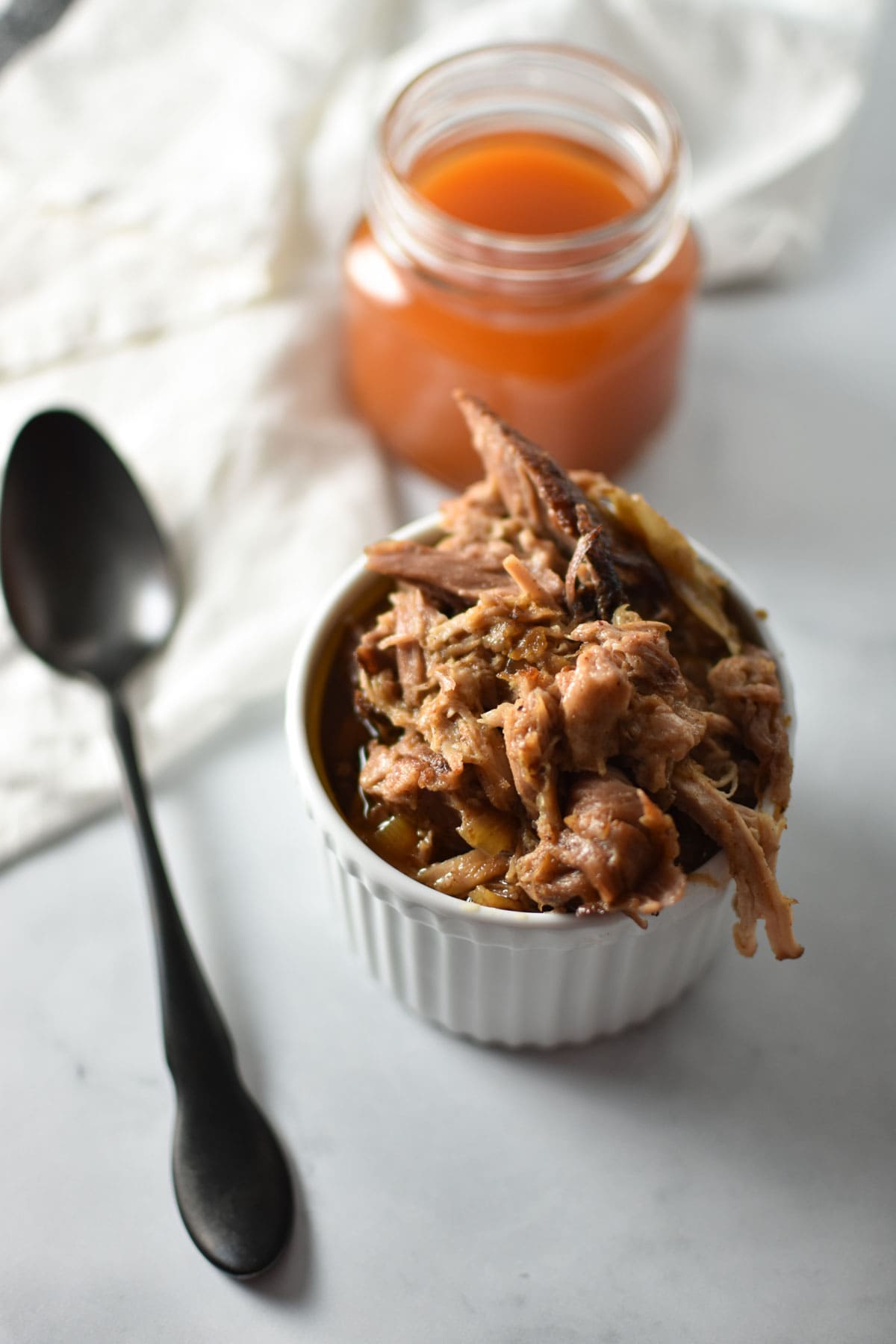 Shredded pork shoulder in a bowl next to vinegar bbq sauce.