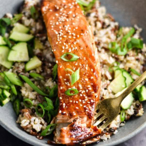 A fork in a fillet of salmon topped with sweet chili sauce.