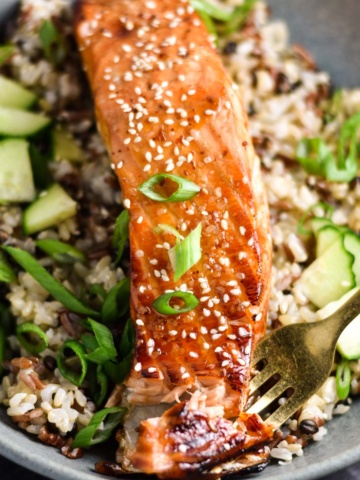 A fork in a fillet of salmon topped with sweet chili sauce.