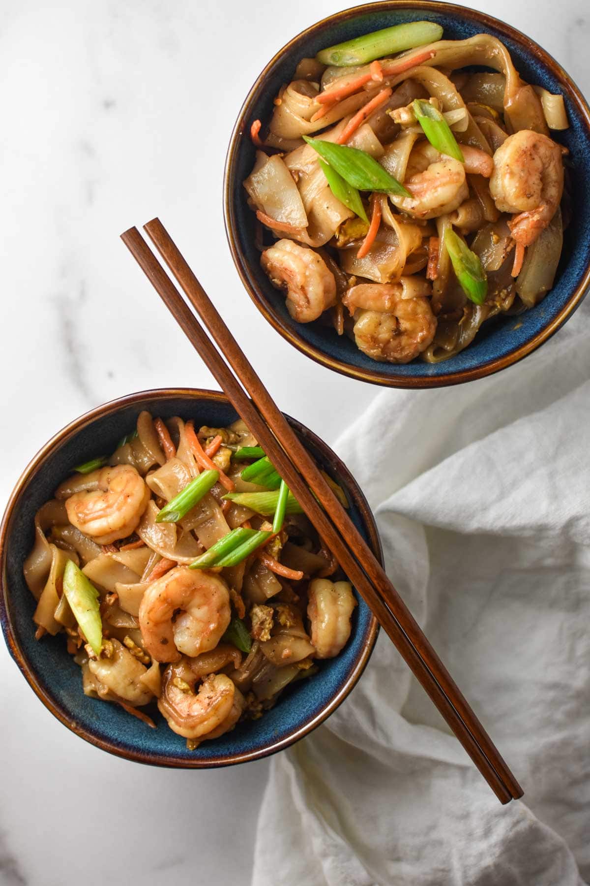 Two bowls of pad Thai with vegetables.