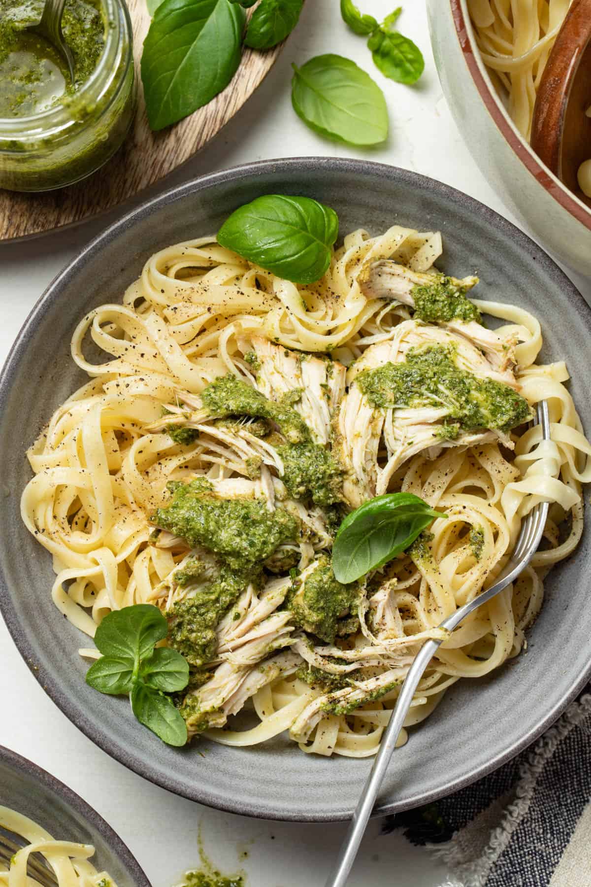 Shredded pesto chicken pasta in a gray bowl with fresh basil on top.