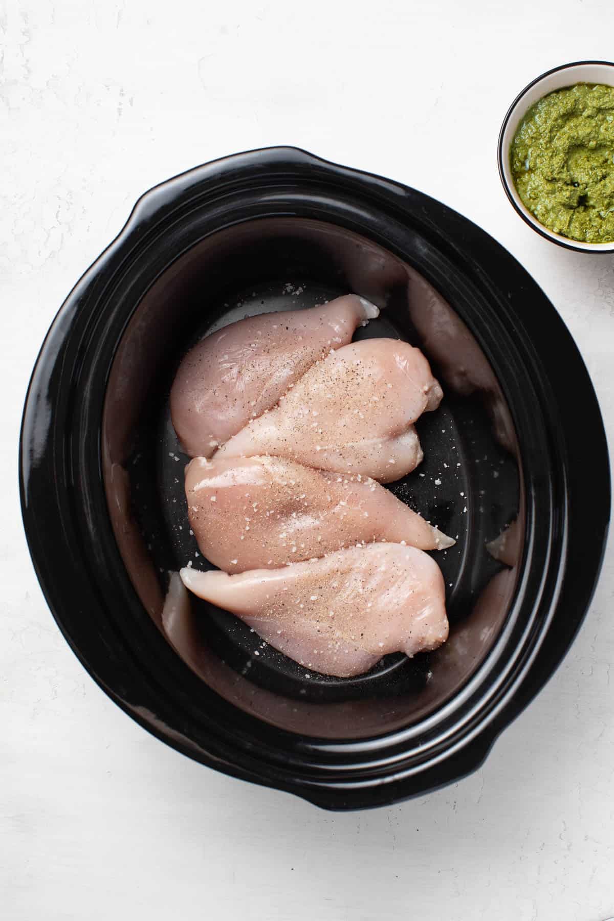 Adding raw, seasoned chicken to the slow cooker.