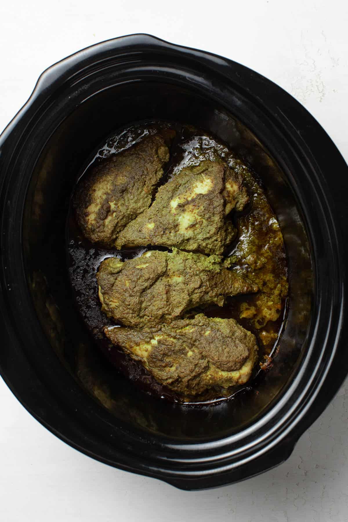 Pesto chicken after being slow cooked, showing how the pesto can brown a bit.