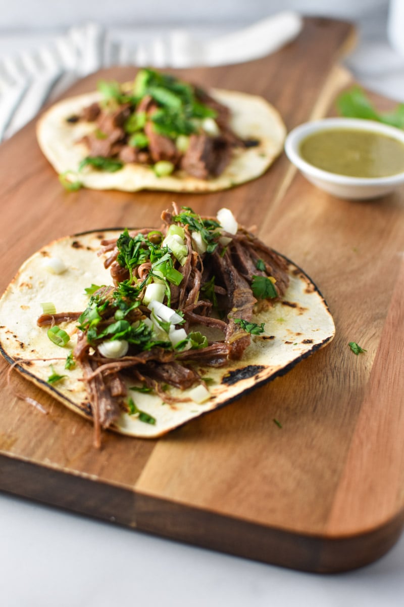 Two steak tacos on a board with salsa verde.
