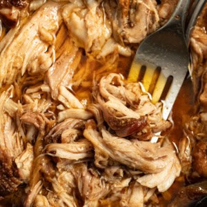 Shredded pork shoulder in a crock pot with a fork.