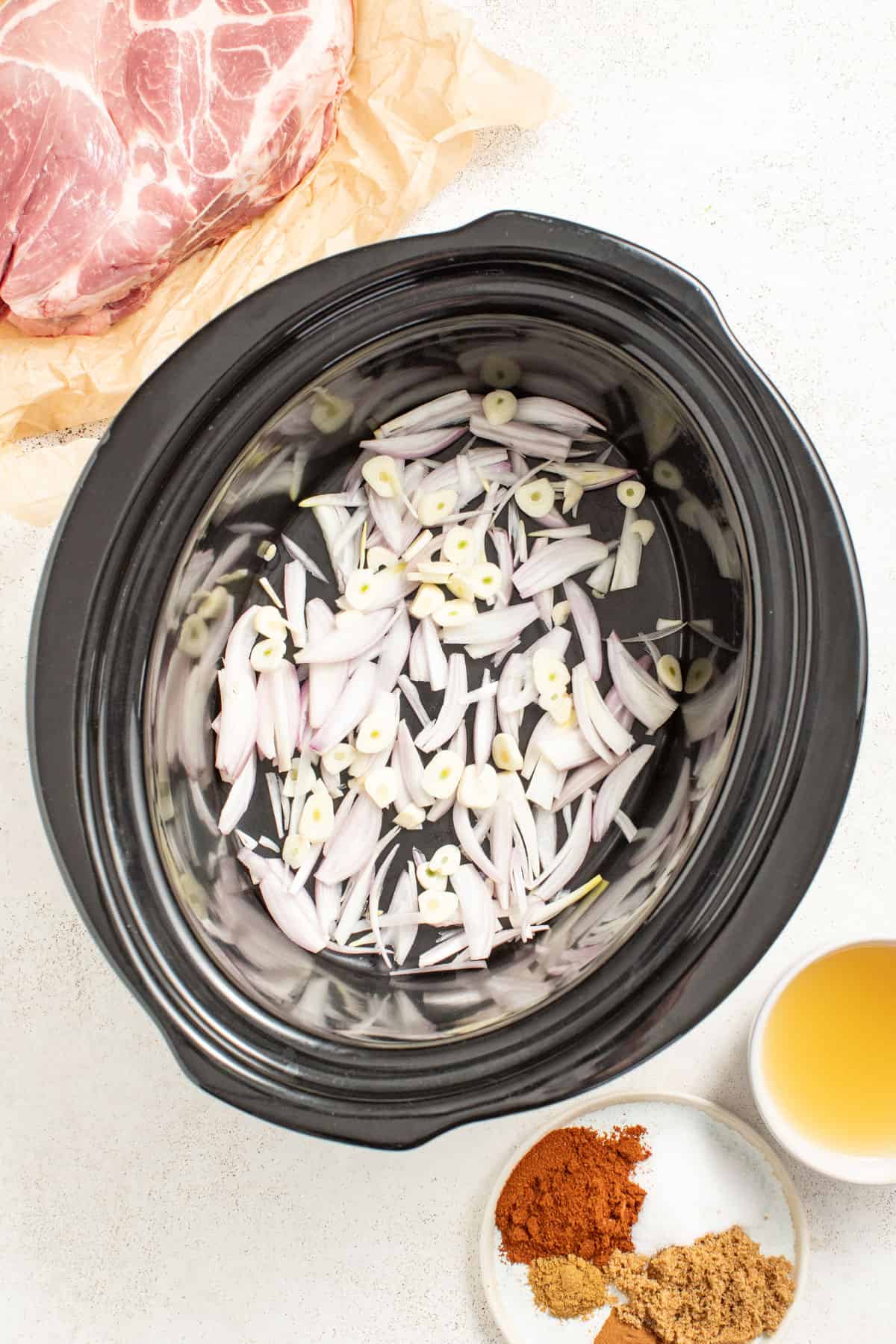 Shallots and garlic in the bottom of a slow cooker.