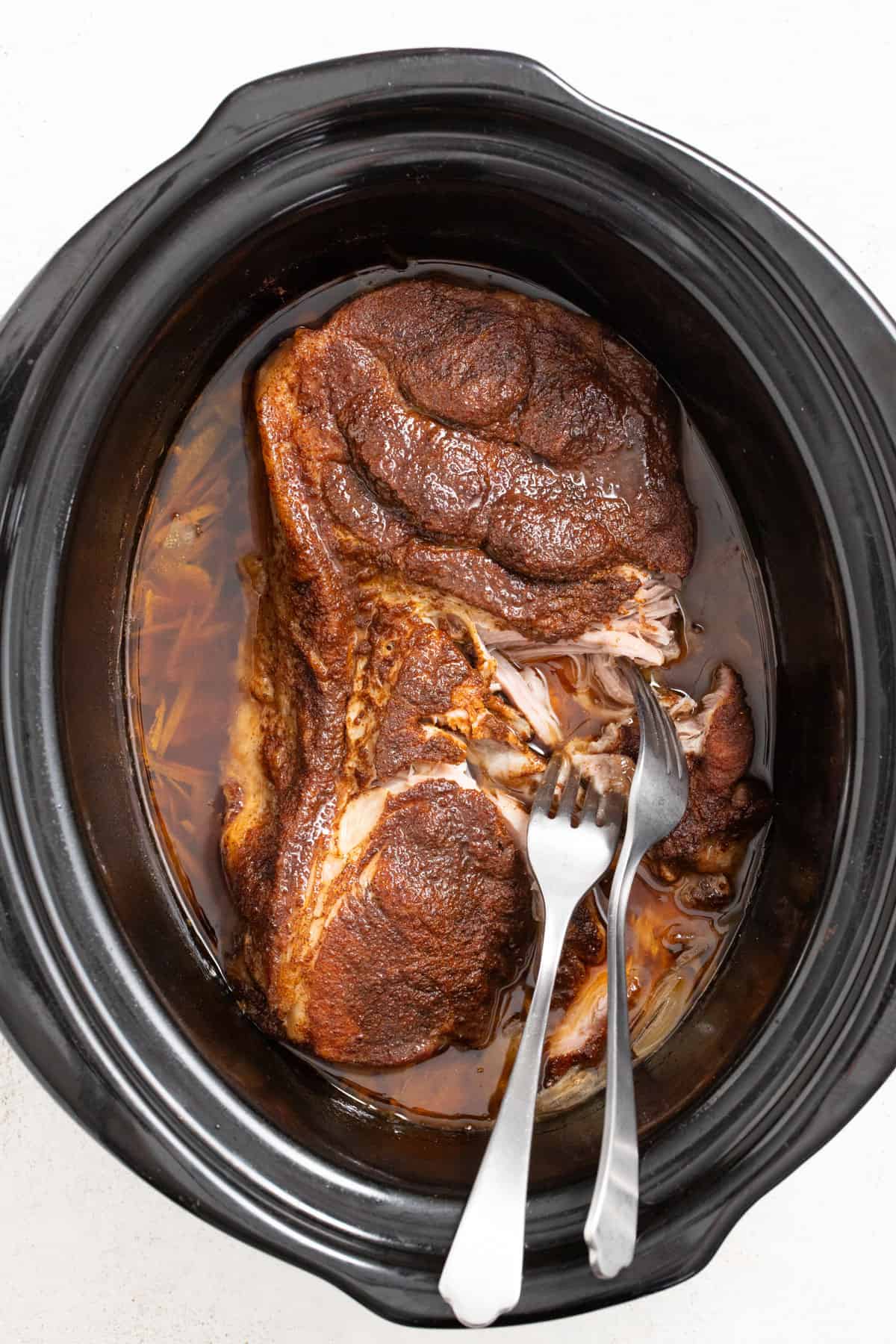 Shredding a cooked pork shoulder in the slow cooker with two forks.