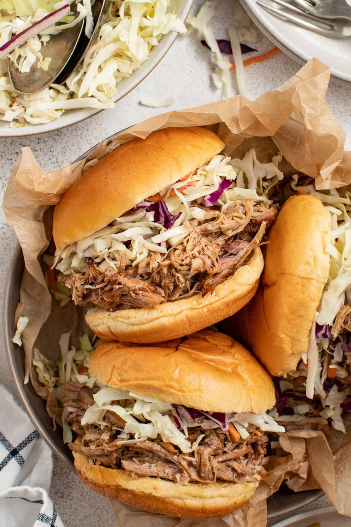 Three pulled pork sandwiches topped with slaw next to shredded pork in a crockpot.
