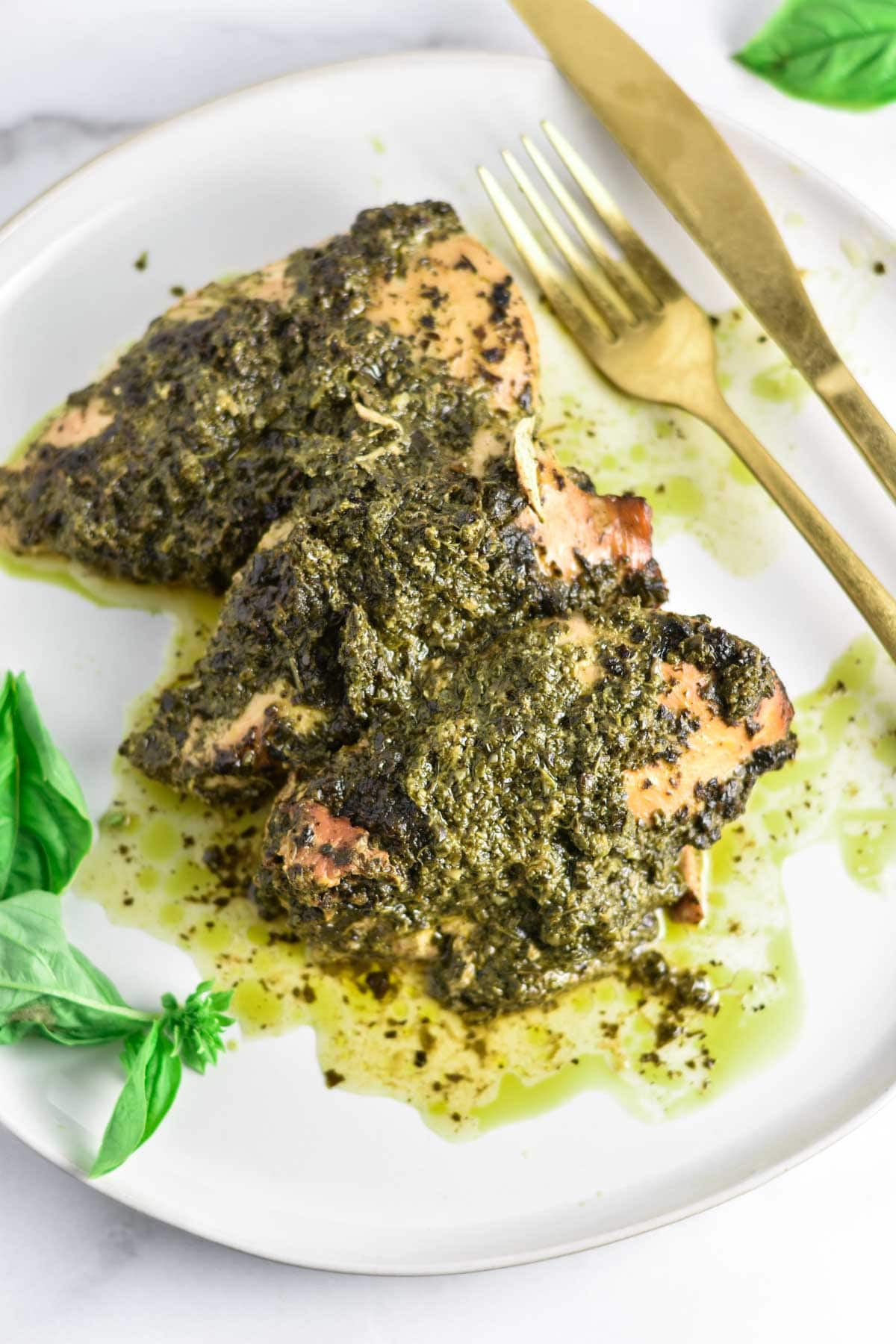A fork and knife next to chicken covered in pesto.