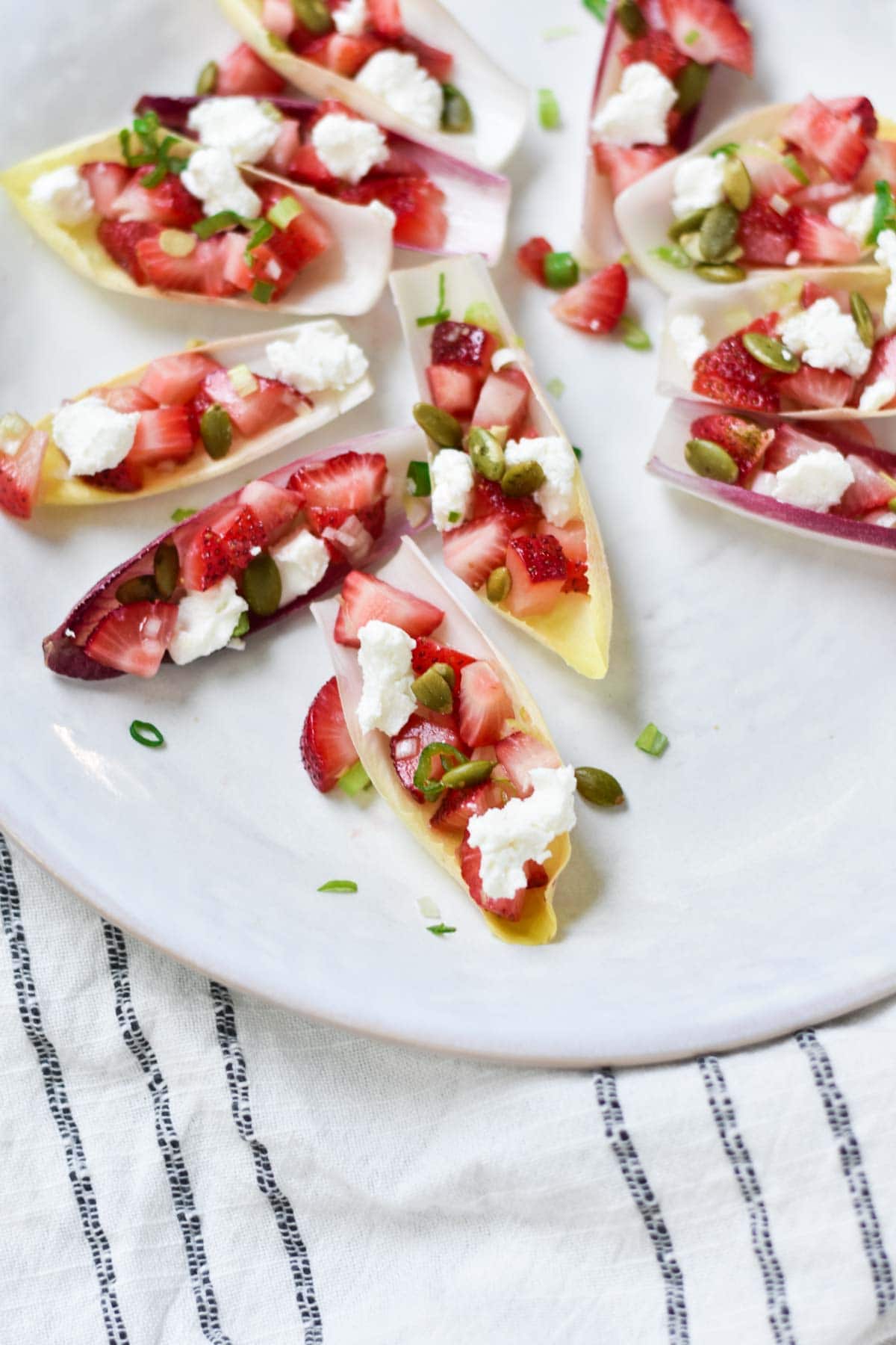 Endive, goat cheese, and strawberries on a plate with a towel.