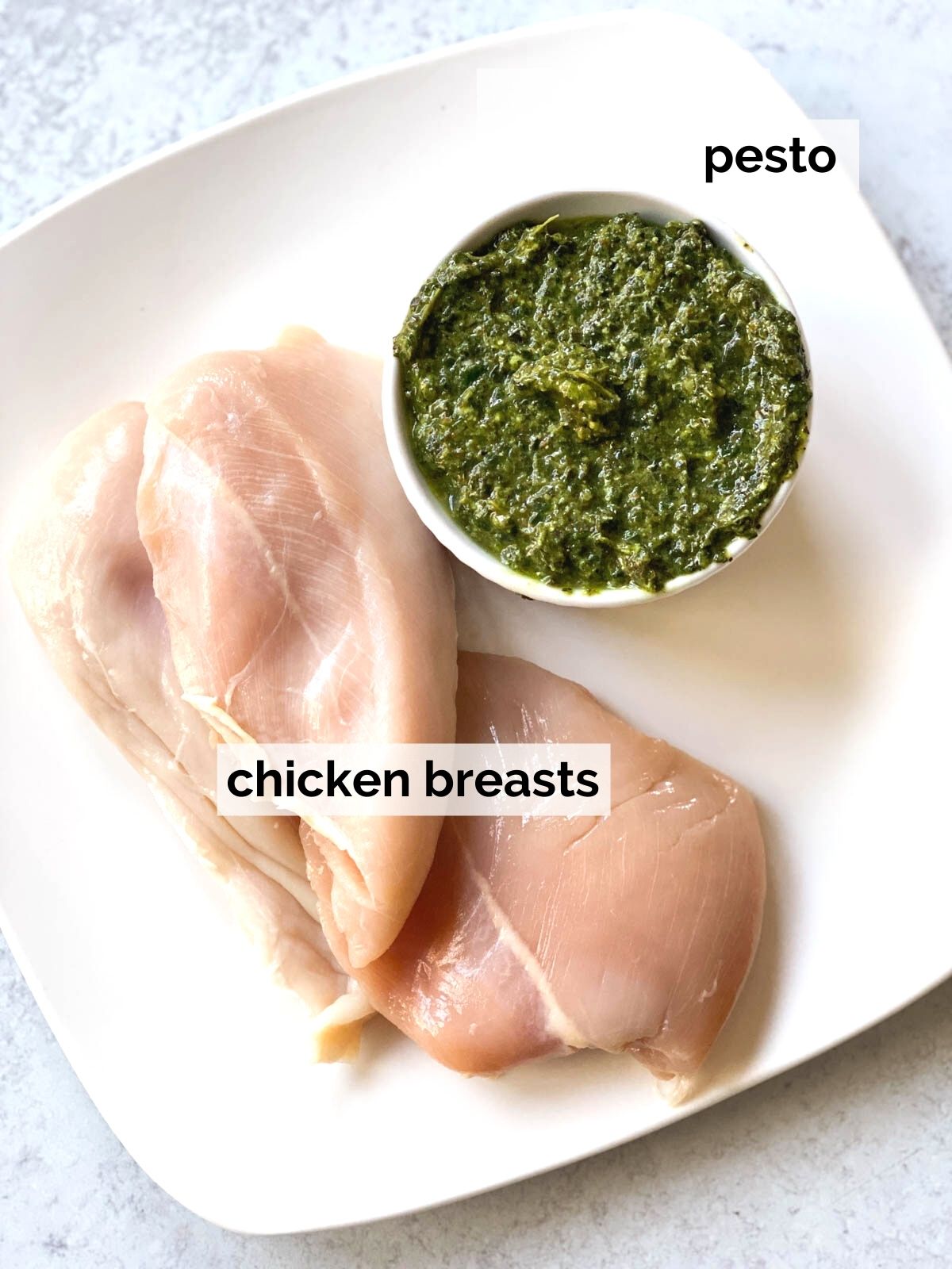 Raw chicken next to pesto on a plate.