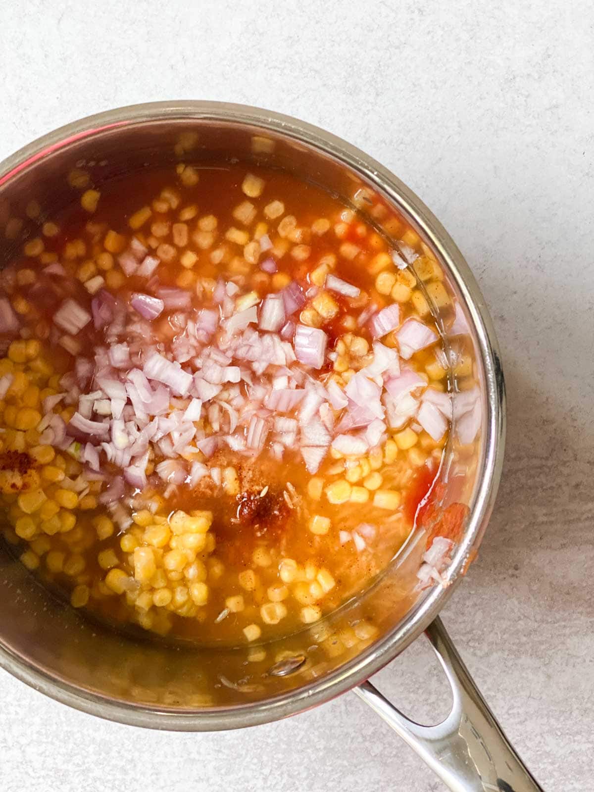 Corn, shallots, tomatoes, and rice in a pot.