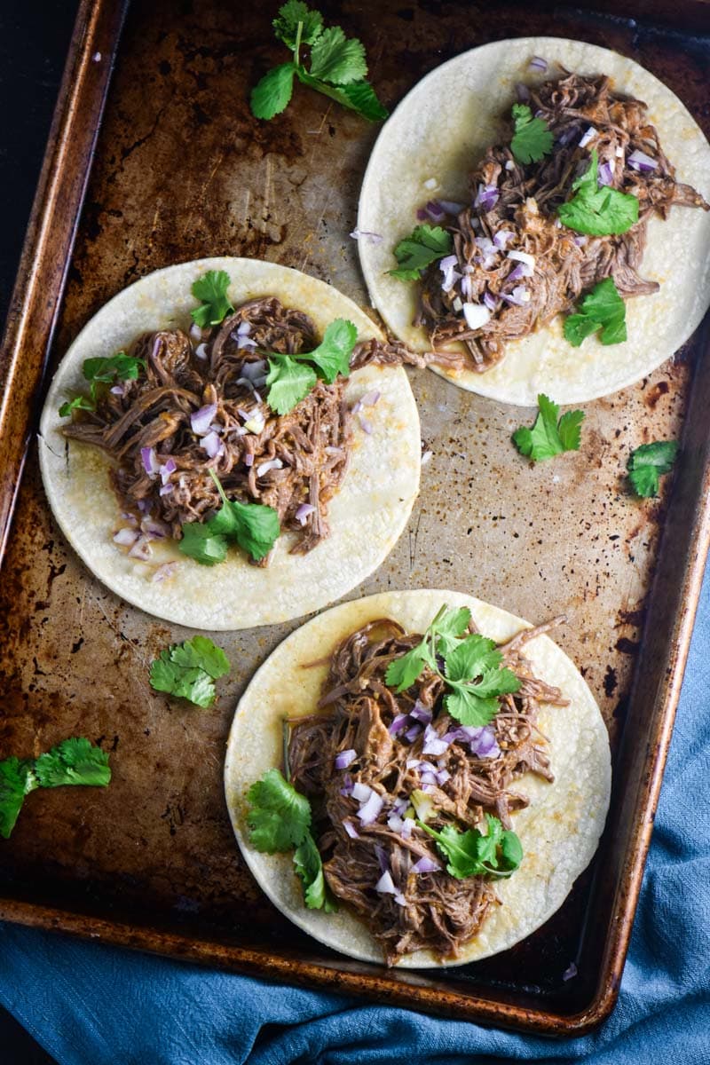 Three tacos with flank steak, cilantro, and shallot.