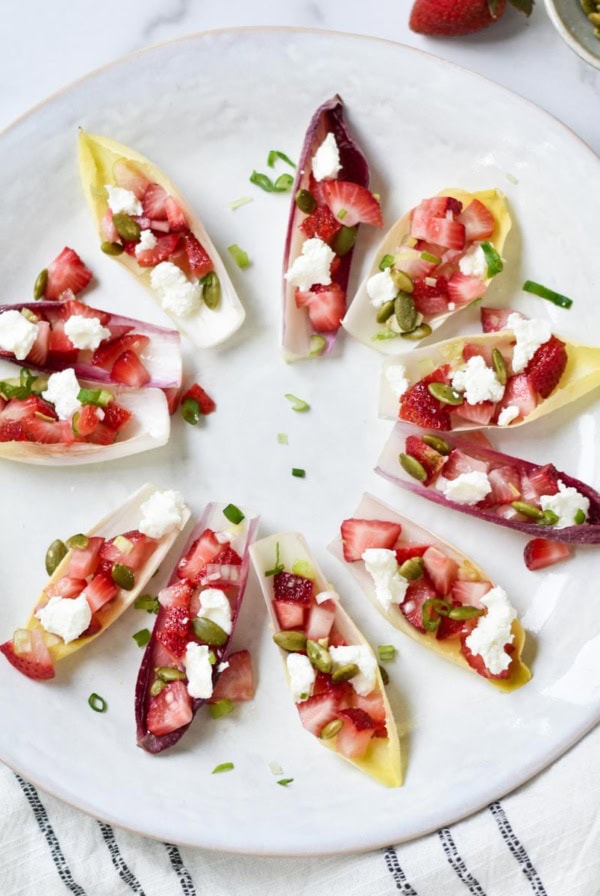Endive appetizer next to green onion, pepitas, and strawberries.