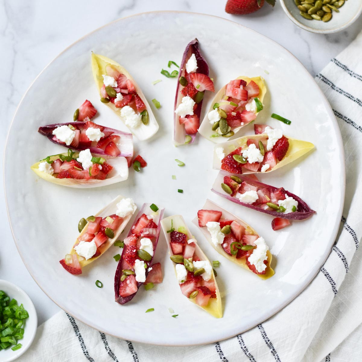 Endive appetizer next to green onion, pepitas, and strawberries.