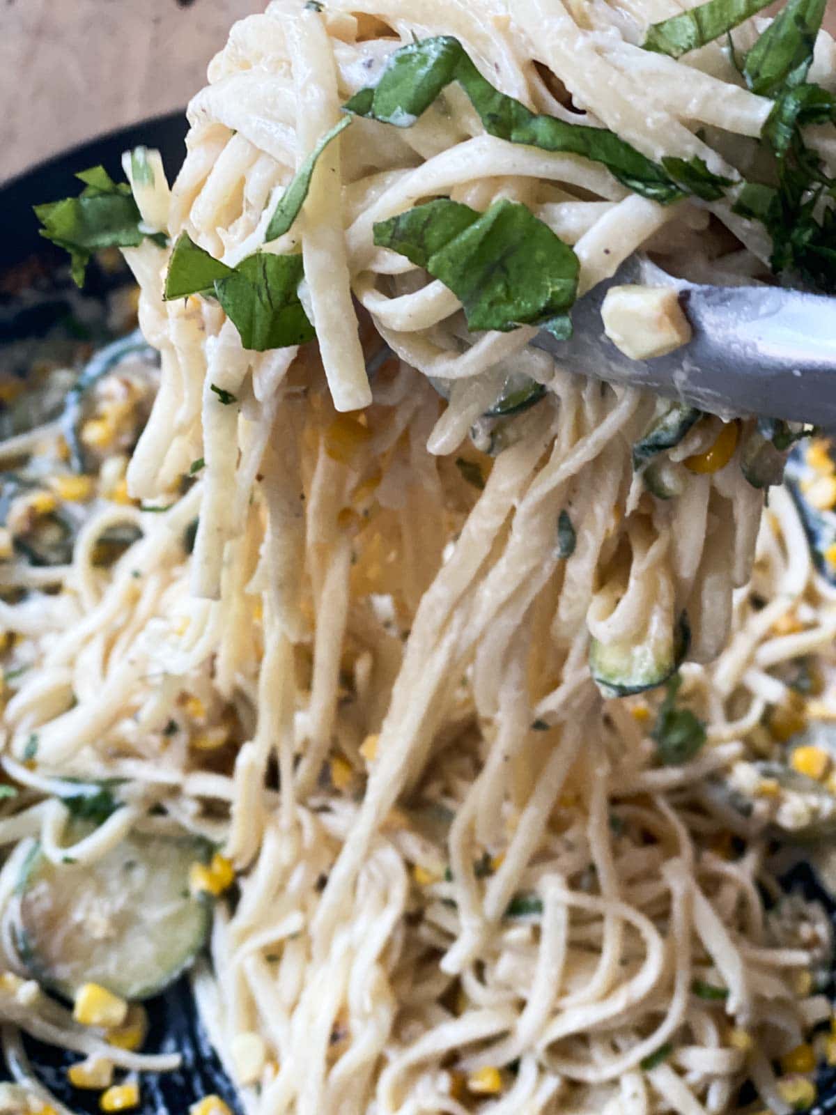 Tongs lifting pasta with basil on top.