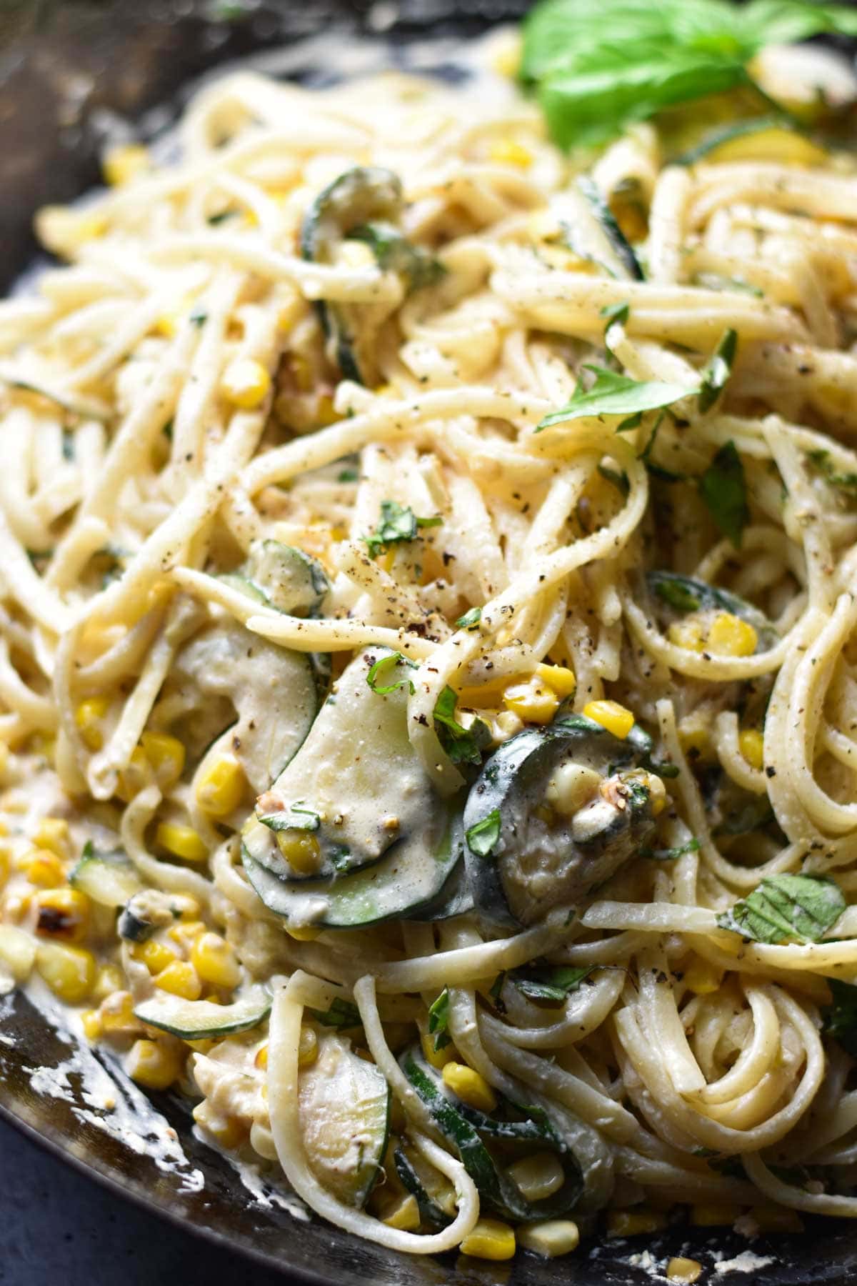 A close up pasta with corn and basil in a cream sauce.