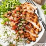 A sliced Mexican spiced grilled chicken breast on top of rice on a white plate.