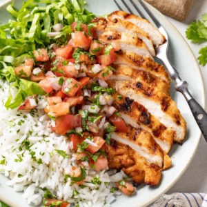 A sliced Mexican spiced grilled chicken breast on top of rice on a white plate.