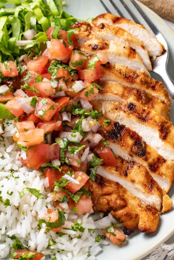 A sliced Mexican spiced grilled chicken breast on top of rice on a white plate.